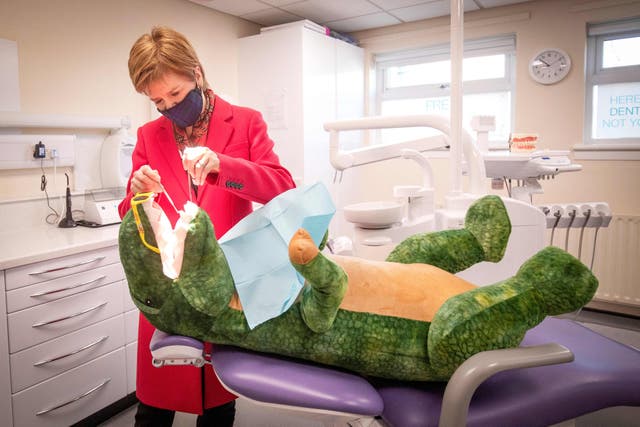Skottlands første minister, Nicola Sturgeon, checks the teeth of "Dentosaurus" under et besøk til Thornliebank tannpleiesenter i Glasgow, som hun kampanjer foran 2021 Skotske parlamentsvalg