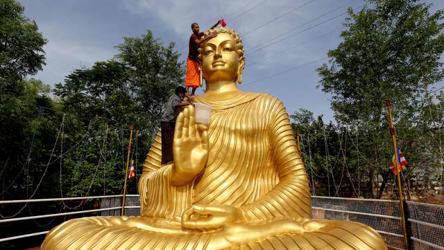 A Buddhist monk climbs atop a giant statue of Buddha, to wash and decorate on the eve of Buddha Purnima, a holiday traditionally celebrated for Buddha's birthday also known as Vesak celebrations, in Bhopal