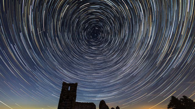 長時間露光写真は、ドーセットのノウルトン教会の廃墟の上で星が円にぼやけるときの地球の自転を捉えています。