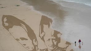 ニューキーのビーチで活動家が砂に引き寄せたG7リーダーの頭を潮が満ちて洗い流し始めると、女性が犬を散歩させます。, コーンウォール