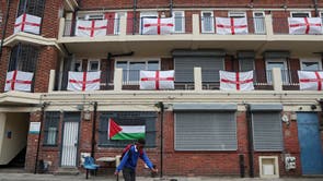 A boy kicks a soccer ball in front of the balconies and landings adorned with predominantly England flags at the Kirby housing estate in London