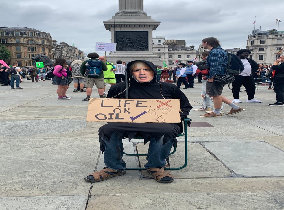 <p>A man wearing a Boris Johnson face mask holds an anti-fossil fuel placard in Trafalgar Square</p>