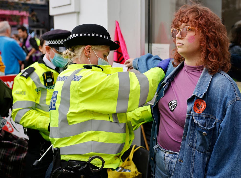 <p>A climate activist from XR is searched by police officers before being arrested </p>