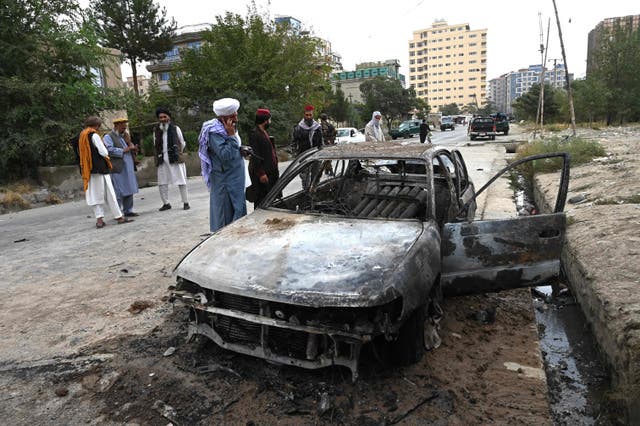 Taliban fighters investigate a damaged car after multiple rockets were fired in Kabul