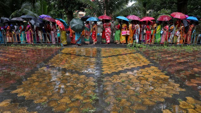 Women hold umbrellas to cover from rain as they wait to receive a dose of COVISHIELD vaccine in Kolkata, インド