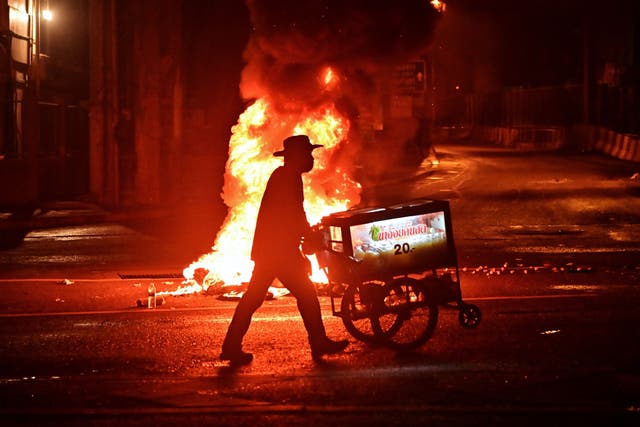 A vendor pushes a cart of sugarcane juice past a fire at a demonstration in Bangkok as activists call for the resignation of Thailand's Prime Minister Prayut Chan-O-Cha over the government's handling of the Covid-19 crisis