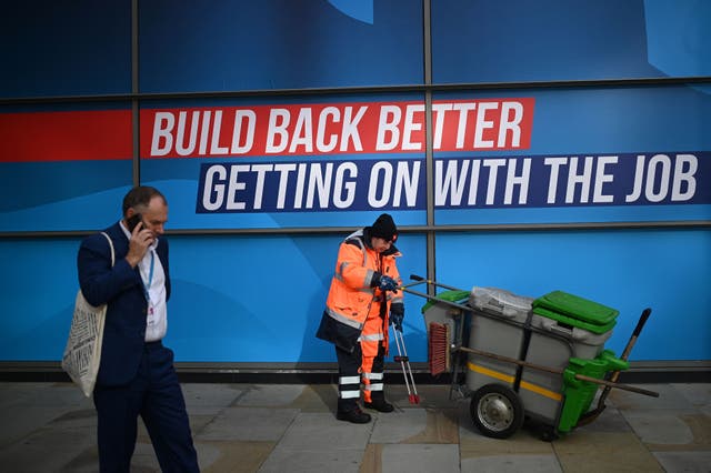 A delegate passes a street cleaner on the second day of the annual Conservative Party Conference being held at the Manchester Central convention centre