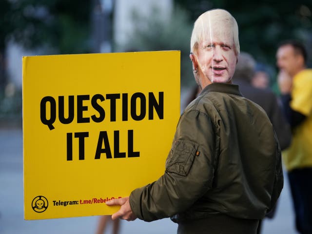  En demonstrant, iført en maske av Johnson, holder et skilt der det står «Question it all» på den siste dagen av Tory-konferansen
