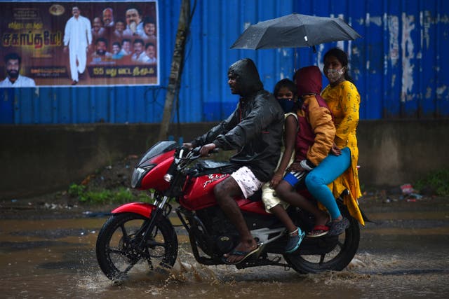 An Indian family rides on a motorcycle as they protect themselves with an umbrella during heavy rain, in Chennai, India