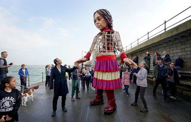 Akteur Jude Law hou hande vas met Little Amal, 'n 3,5 meter hoë marionet van 'n negejarige Siriese meisie, soos dit in Folkestone aankom, Kent, as deel van die Handspring Puppet Company se 'The Walk'