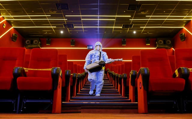 A worker wearing personal protective equipment sanitises seats inside a movie theatre ahead of its reopening in Mumbai, India