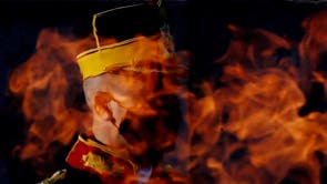 An honour guard soldier wearing a protective mask stands at attention, as seen through the eternal flame, at the Unknown Soldier Memorial, during the Romanian Army Day celebration, in Bucharest, Romania