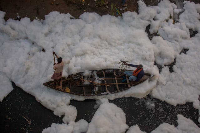Un homme rame un bateau sur la rivière Yamuna, recouvert d'une mousse chimique causée par la pollution industrielle et domestique, pendant le festival Chhath Puja à New Delhi