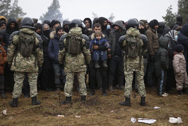 Migrants stand in front of Belarusian servicemen as they gather in a camp near the Belarusian-Polish border in the Grodno region