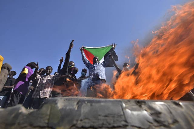 A man holds a Sudanese national flag before flames at a barricade as people protest against the military coup in Sudan, 在 "Street 60" in the east of capital Khartoum