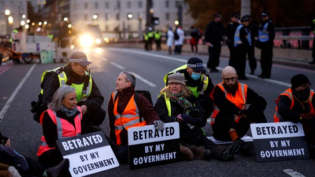 Police officers monitor as climate change activists sit down and block traffic during a protest action in solidarity with activists from the Insulate Britain group who received prison terms for blocking roads, on Lambeth Bridge in central London