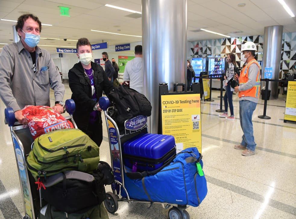 <p>Travellers with their luggage walk past the Covid-19 Testing location at the airport in Los Angeles, California on 23 November 2021</p>