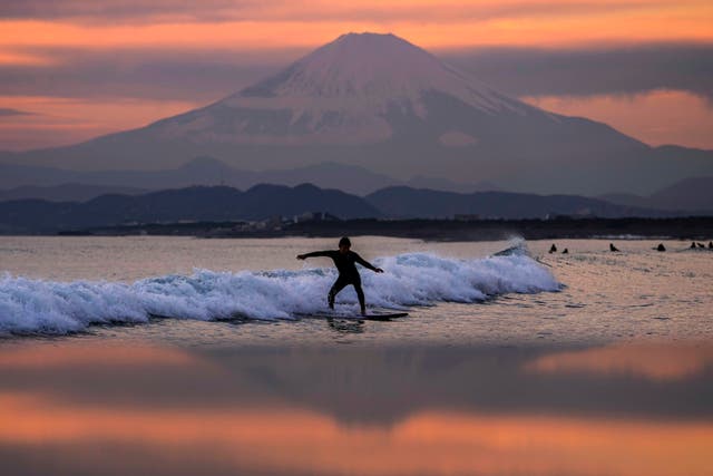 A surfer rides a wave in front of iconic Mount Fuji as the sun sets in Japan