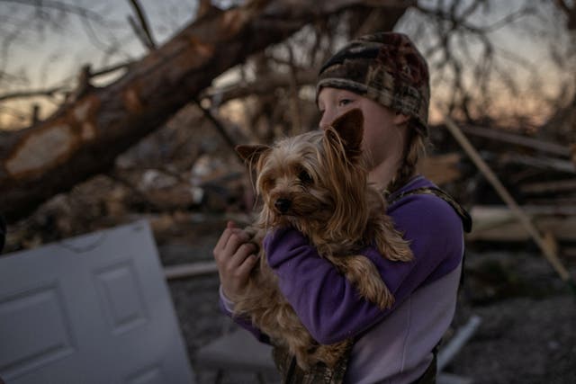 Braelyn Todd, 8, holds her dog Abner, a Yorkshire Terrier, as her parents help a family member clear debris from their destroyed home in the aftermath of a tornado in Mayfield, Kentucky
