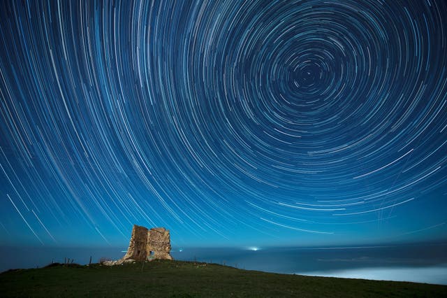 An overlay image of 128 photographs shows circumpolar star trails over San Telmo tower in Ubiarco, Spanje