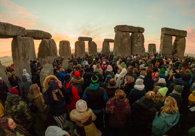 O sol nasce atrás das pedras enquanto as pessoas se reúnem para o solstício de inverno em Stonehenge.