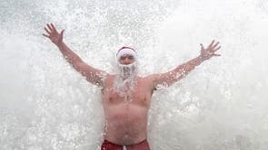 Patrick Corkery wears a santa hat and beard as waves crash over him at Forty Foot near Dublin during a Christmas Day dip