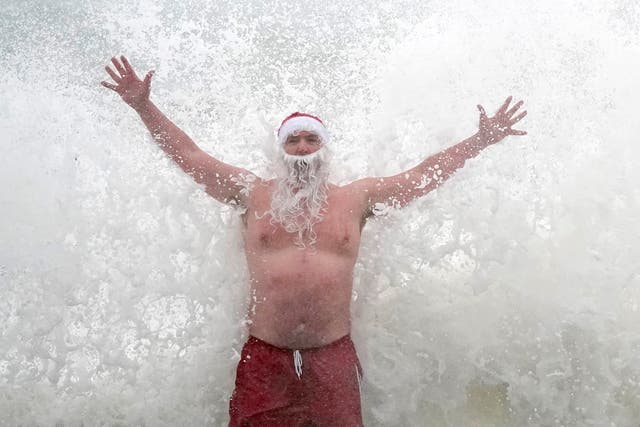 帕特里克·科克里（Patrick Corkery）戴着圣诞老人的帽子，留着胡须，在圣诞节期间，在都柏林附近的四十英尺，海浪拍打着他