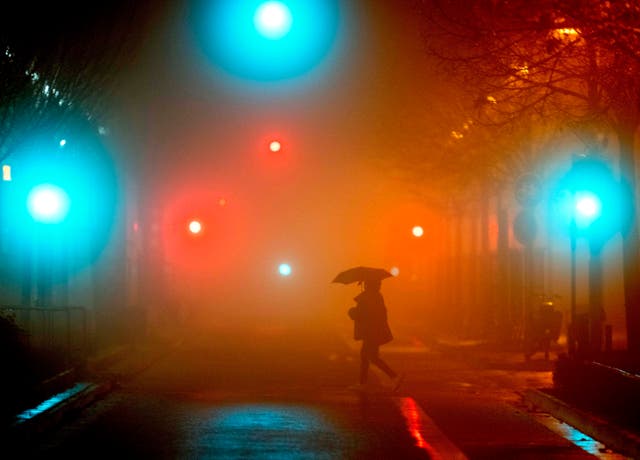 A man crosses a street in Frankfurt, 德国, on a rainy and foggy morning