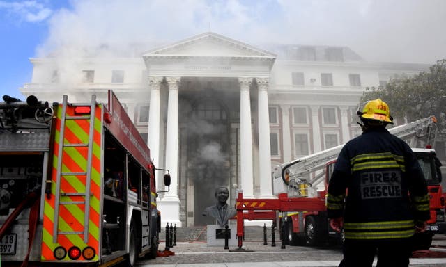 A firefighter looks at the smoke rising after a suspected arson in the Parliament in Cape Town, África do Sul