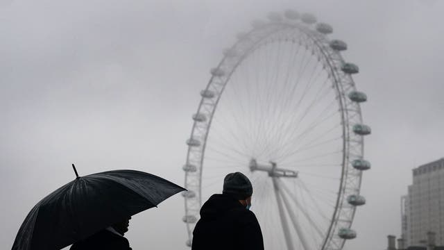 在伦敦市中心威斯敏斯特桥的潮湿天气里，一对夫妇在雨伞下散步