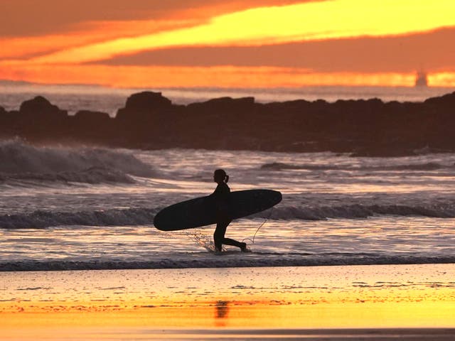 Les surfeurs entrent dans la mer alors que le soleil se lève sur Tynemouth sur la côte nord-est