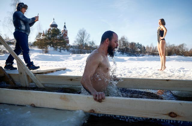 A woman poses for a picture near an ice hole as a man takes a dip during celebrations of the Orthodox Christian feast of Epiphany in the settlement of Ivanovskoye in the Moscow region, Russia