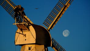 Willesborough Windmill, a white smock mill built in 1869 is bathed in the morning sunshine as the moon sets behind in Ashford, Kent