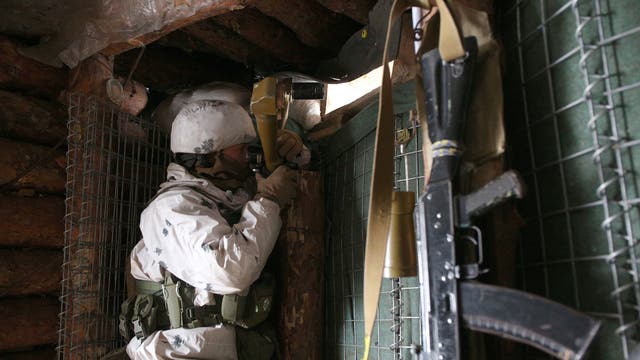 An Ukrainian Military Forces serviceman, watches through spyglass in a dugout on the frontline with Russia-backed separatists near Gorlivka, Donetsk region