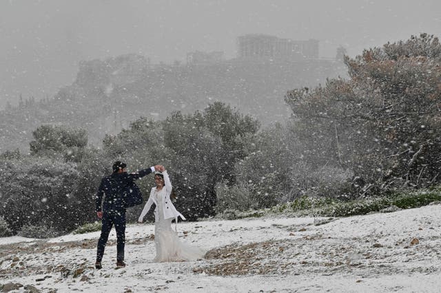 A newlywed couple from the US enjoys a snowfall during a photo shooting near the Acropolis in Athens