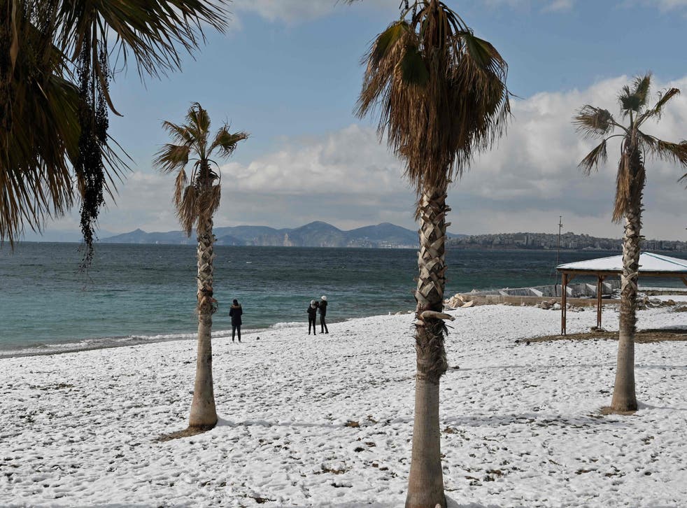 <p>People walk along a snow-covered beach in Athens</p>