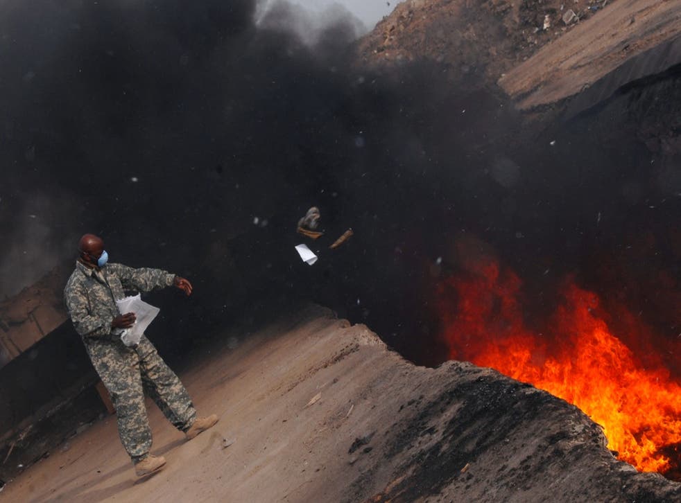 <p>A US service member throws trash into a huge burn pit  </p>