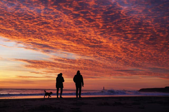 Passeadores de cães apreciam o nascer do sol da manhã em Tynemouth Beach em North Tyneside, na costa nordeste da Inglaterra