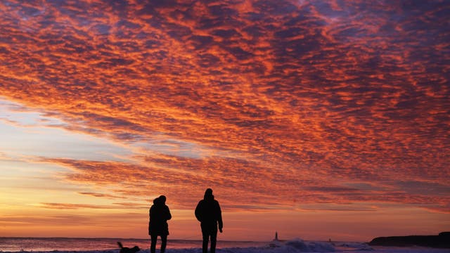 Dog walkers enjoy the early morning sunrise at Tynemouth Beach in North Tyneside, on the north east coast of England