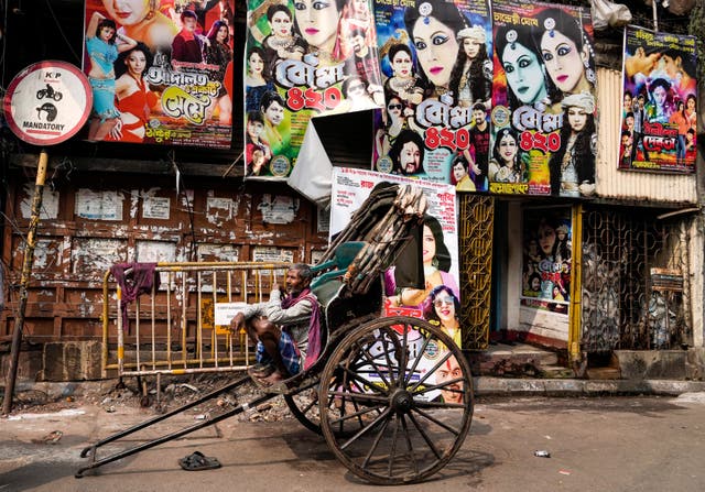 An Indian hand rickshaw puller waits for customers in front of a building displaying posters of different theater shows in Kolkata, Indië