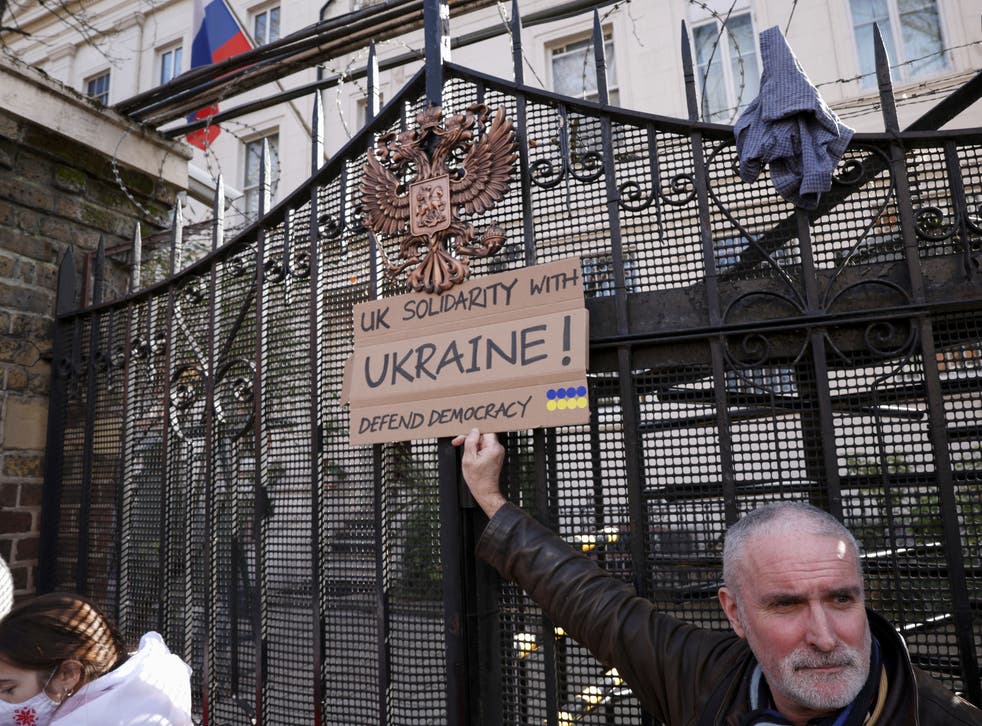 <p>A protester holds a sign in front of the gate of the Russian embassy during an anti-war protest in London</p>