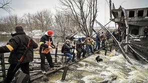 Members of an Ukrainian civil defense unit pass new assault rifles to the opposite side of a blown up bridge on Kyiv’s northern front
