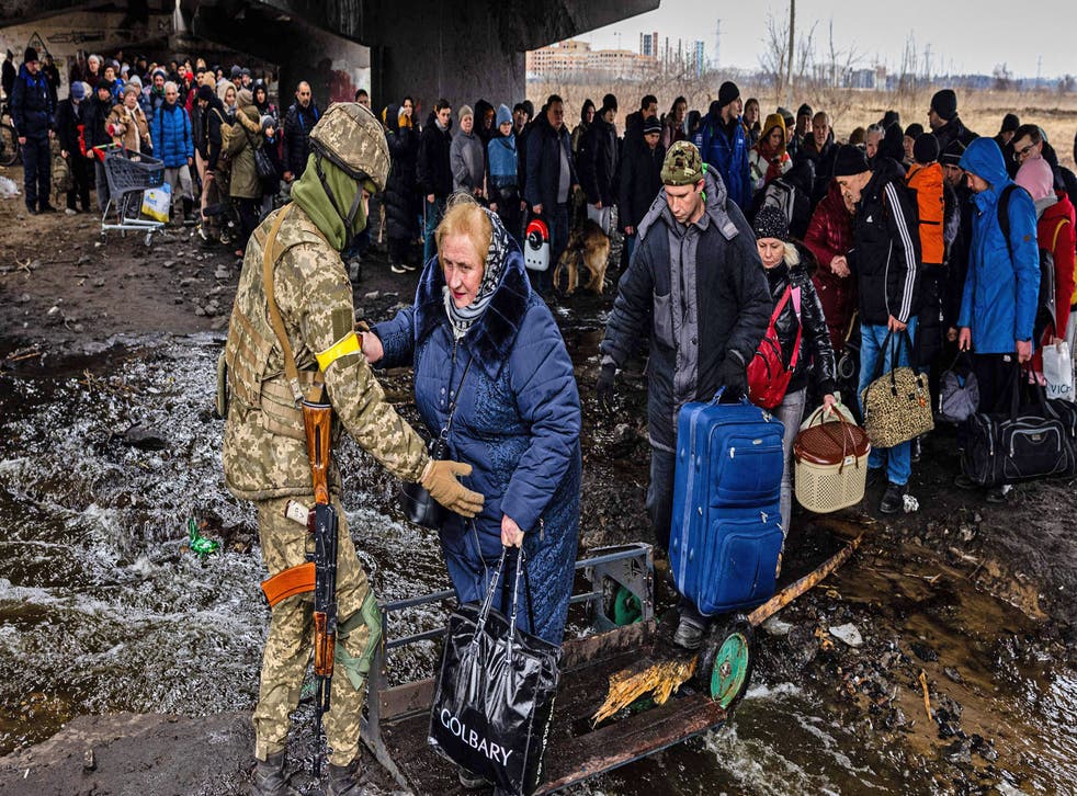 <p> A Ukrainian serviceman helps evacuees gathered under a destroyed bridge, as they flee the city of Irpin, northwest of Kyiv, on 7 March</p>