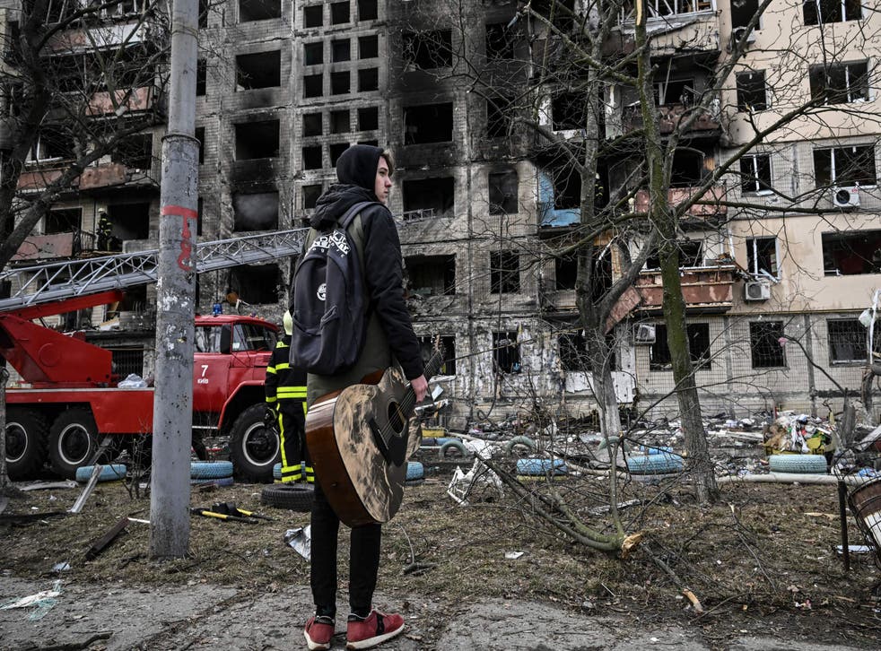 <p>Maksim Korobych, 18-years-old, holds his guitar as he stands in front of his destroyed apartment building</p>
