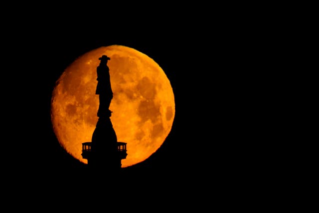 The moon sets behind a statue of William Penn atop of City Hall in Philadelphia
