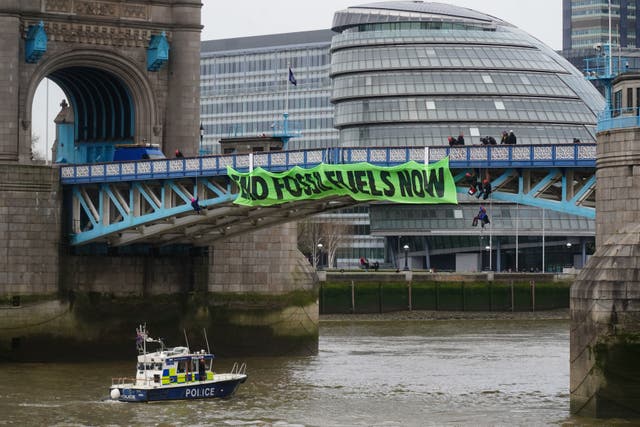 Police officers work to remove activists from Extinction Rebellion who were hanging from suspension cords beside a giant banner that reads “End fossil fuels now”, as they stage a protest on Tower Bridge, Leste de Londres, which has been closed to traffic