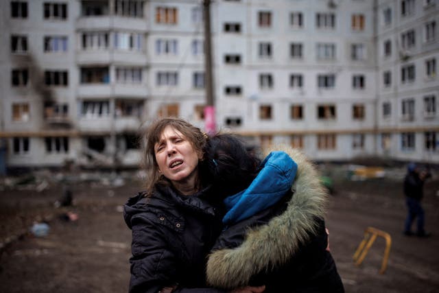 Two women hug outside a heavily damaged apartment block following an artillery attack during the Russian assault on Kharkiv
