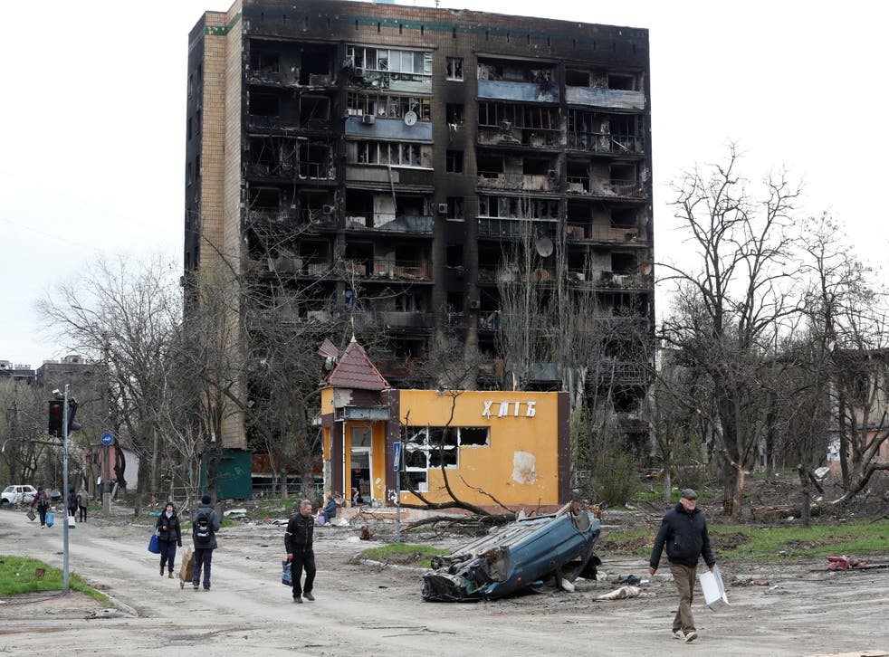 <p>People walk past a residential building heavily damaged during Ukraine-Russia conflict in the southern port city of Mariupol, Ukraine 21 April 2022</p>