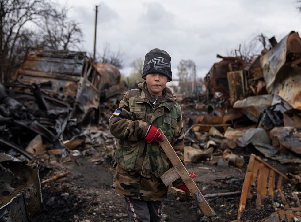 <p>A boy holds a wooden toy rifle next to destroyed Russian military vehicles near Chernihiv</s>