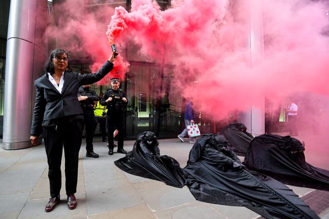 A demonstrator holds a pink smoke flare billowing over members of Extinction Rebellion staging a protest against the use of and investment in fossil fuel, outside offices of Vanguard Asset Management on Earth Day in the City of London